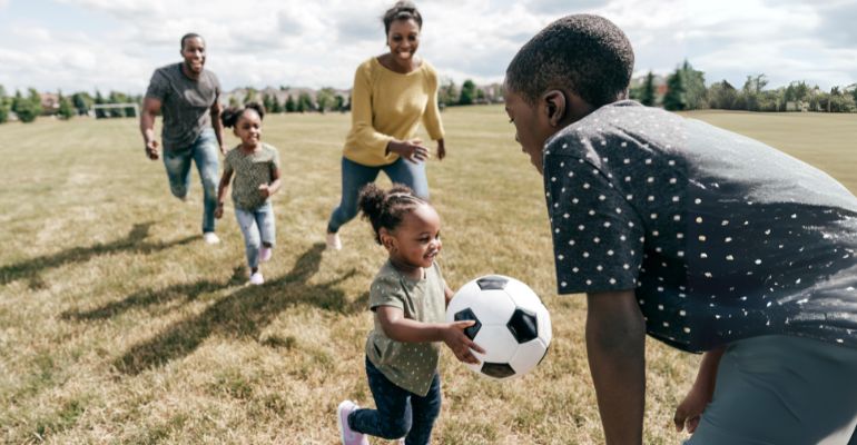 Family playing soccer in a park