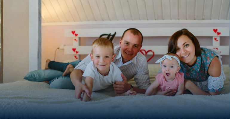 A family of four laying on a bed smiling