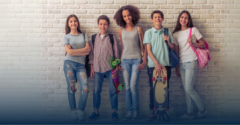 group of five young teenagers standing against a wall smiling